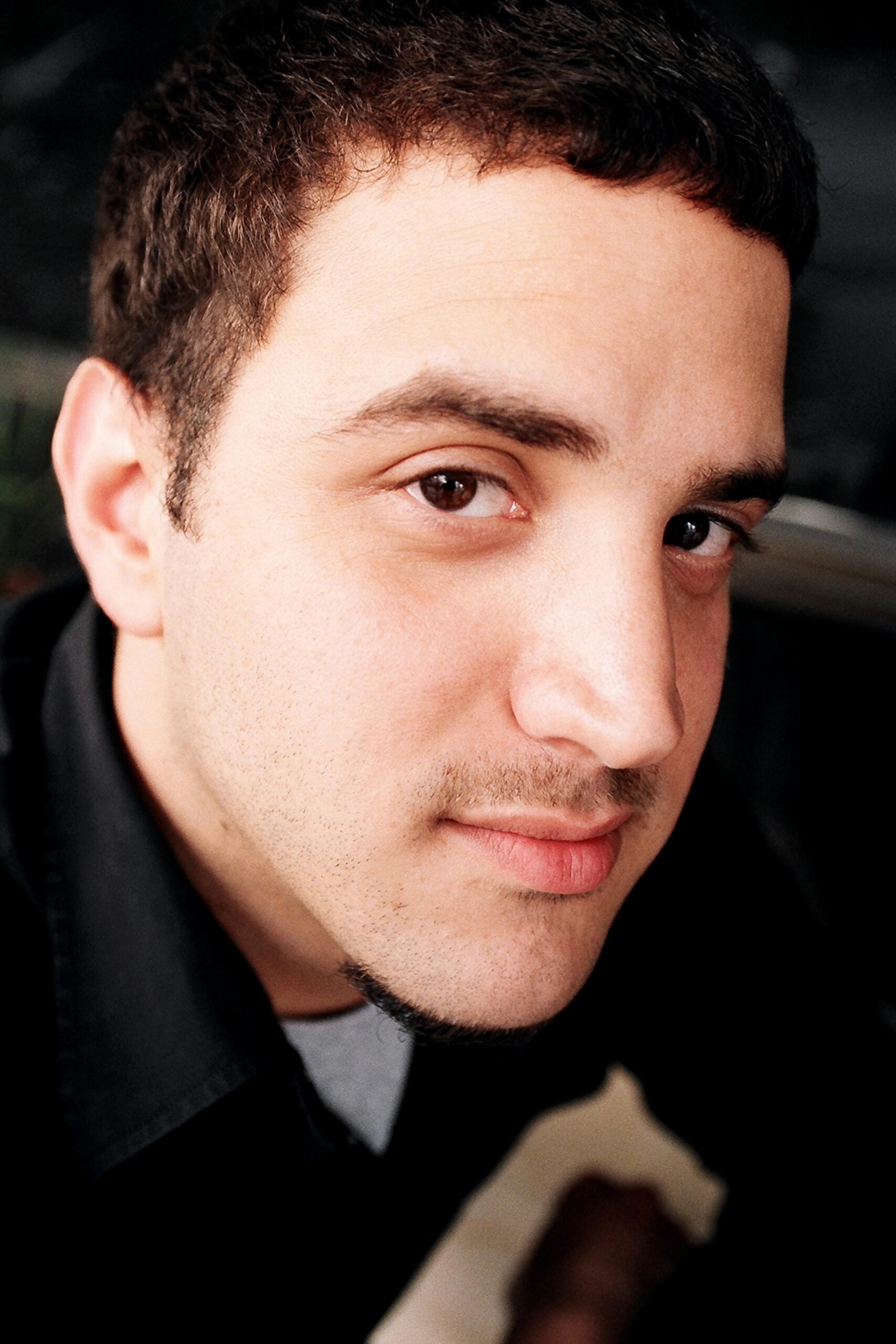 Acasă A close-up portrait of a young man with a soft, intense gaze, under natural lighting in an urban setting.
