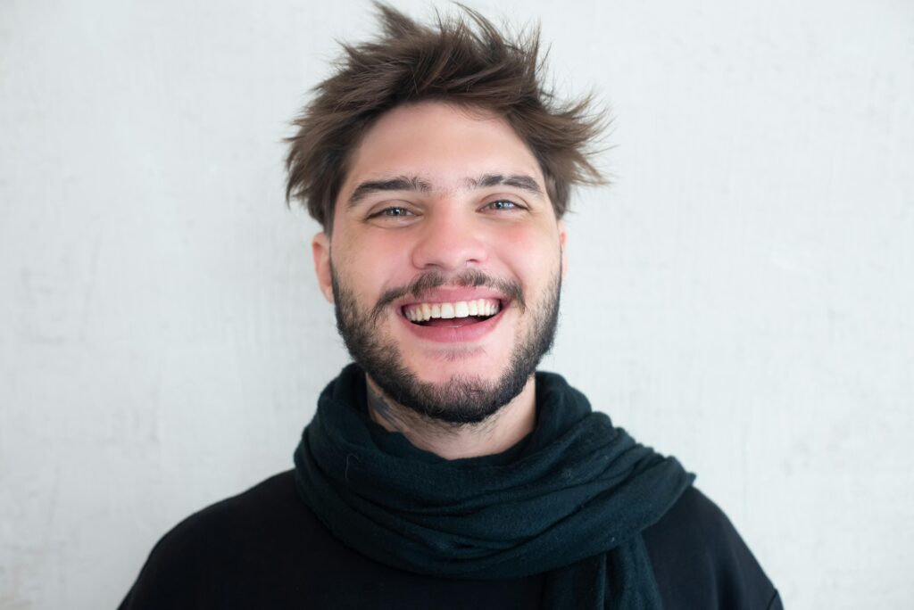Acasă Cheerful young man with a beard smiling warmly, wearing a scarf.